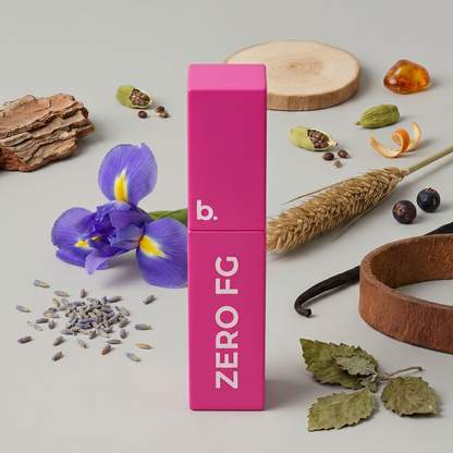 A bright pink rectangular box labeled 'b. ZERO FG' stands upright on a light gray surface, surrounded by styled natural props including a purple iris flower, lavender buds, dried leaves, a wheat stalk, wood slice, and small seeds.